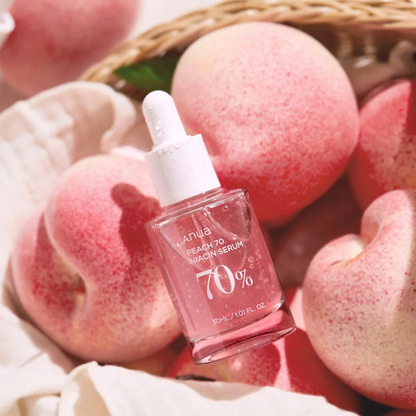 Close-up of Anua Peach 70% Niacinamide Serum bottle with fresh peaches in the background, showcasing natural skincare ingredients.