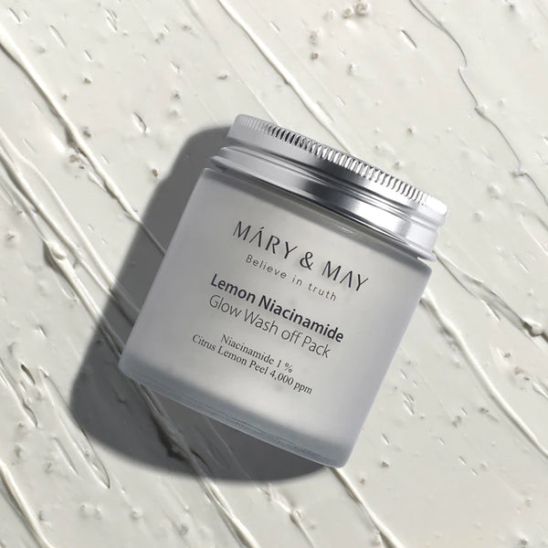Frosted jar of MARY & MAY Lemon Niacinamide Glow Wash Off Pack on a textured white surface, evoking a clean and fresh skincare theme.