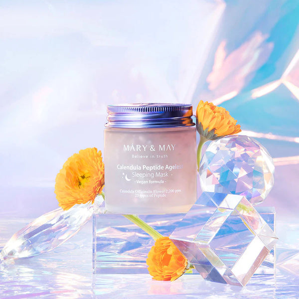 Artistic display of MARY & MAY Calendula Peptide Ageless Sleeping Mask with vibrant marigold flowers and iridescent crystals, showcasing the product's natural ingredients.