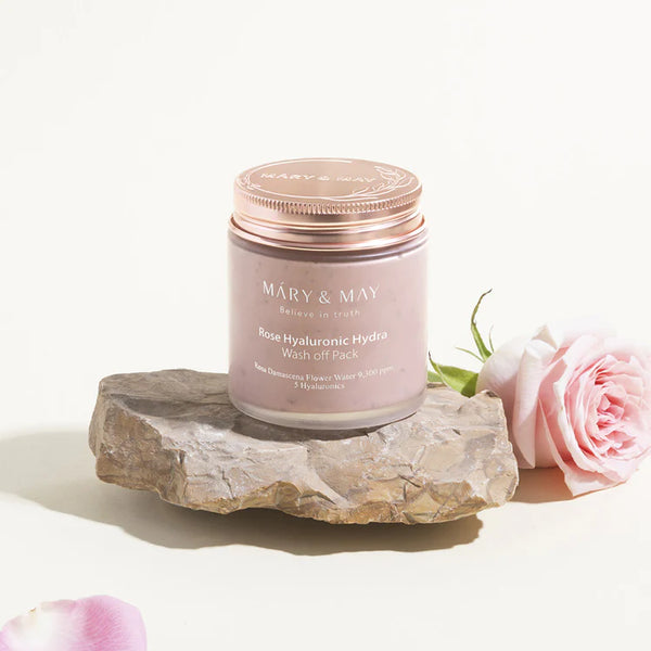 MARY & MAY Rose Hyaluronic Hydra Wash Off Pack on a natural stone, next to a blooming pink rose, symbolizing the natural ingredients used.