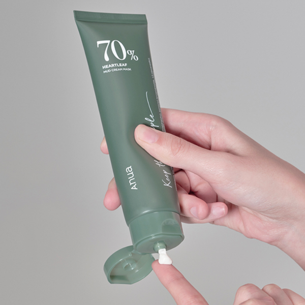 hand squeezing creamy anua 70% heartleaf mud cream mask out of its dark green tube onto finger.