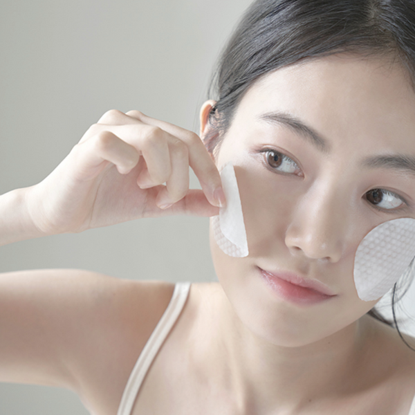 Woman placing cotton pads soaked in anua heartleaf soothing toner on face.