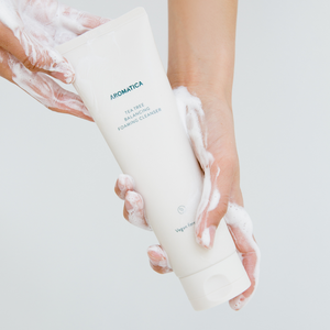 Hands covered in foamy Aromatica tee tree balancing foaming cleanser holding beige bottle of the cleanser