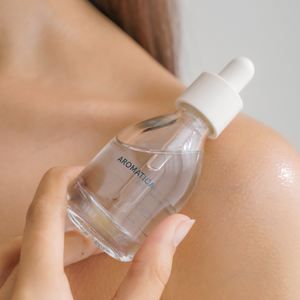 Hand holding small glass bottle of aromatica tea tree oil next to bare shoulder