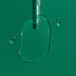 Aromatica Tea Tree Oil coming out of glass dropper on green background