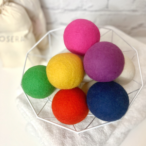 Six multicolor wool dryer balls in white basket. Wool ball colors shown are pink, purple, yellow, green, orange, and blue.