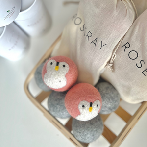 baby pink penguin wool dryer ball and four gray wool dryer balls with cotton roseray bags